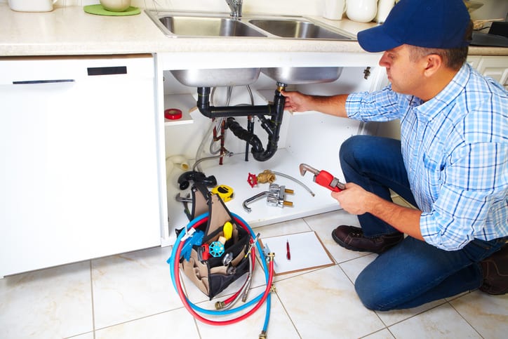 Image of a man fixing a sink who uses a plumbing answering service