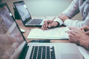 Image of laptops, paper, pens, and two people creating a business phone script