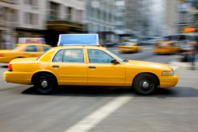 Image of a taxi driving through the city to pick up a passenger who called a taxi answering service