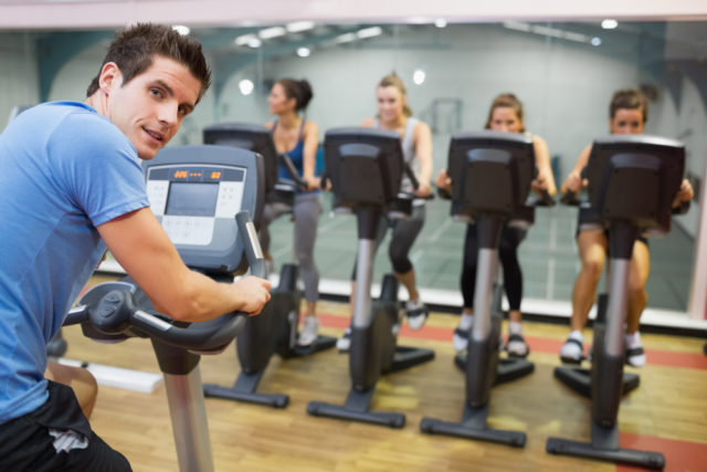 Image of a man leading a fitness class while the gym answering service handles phone calls