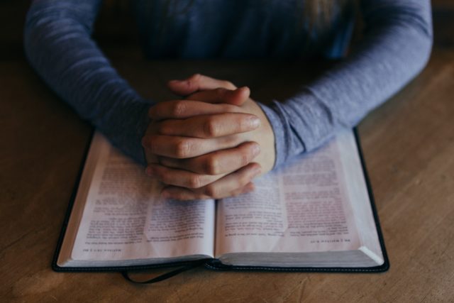 person with their hands folded over the good book in prayer after calling a church answering service