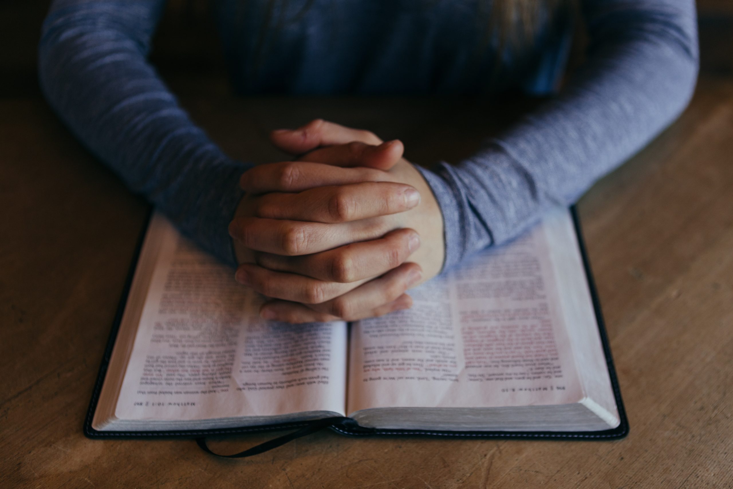 image of a person with their hands folded over the good book in prayer