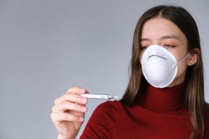 woman in a mask reading her temperature on a thermometer