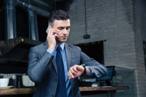 Businessman looking at his watch and using phone forwarding