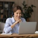 woman with headset on at desk looking at her laptop