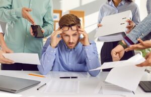 stressed at desk with people handing things